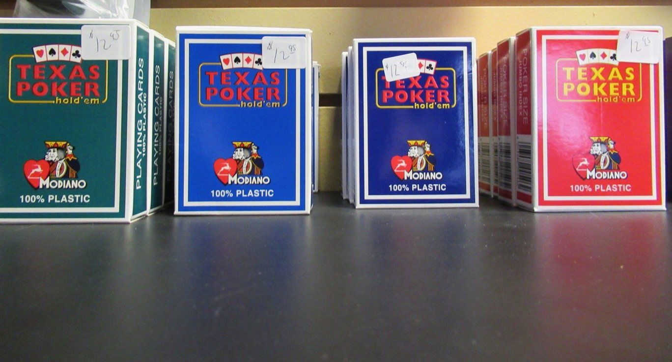 Assorted Texas Poker playing card boxes lined up on a dark surface, in green, blue, and red packaging