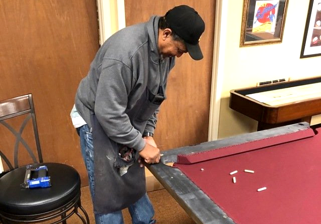 Man adjusting the corner pocket of a red pool table in a wood-paneled room