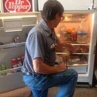 Store Signage — Appliance Repair in Collins, CO Man sitting on a kitchen stool facing an open refrigerator with drinks and snacks inside