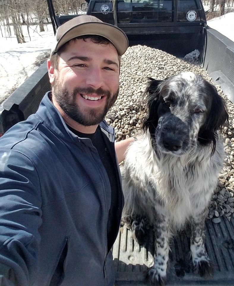 Jeff and Lexi at Off The Beaten Trail Canine Facility in Newark, VT Jeff wearing a blue jacket posing with a black and white dog in the bed of a truck