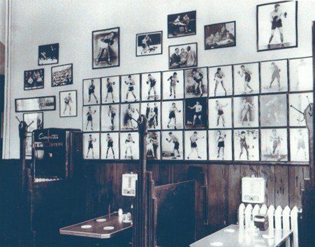 A wall inside a restaurant or bar is covered with a large grid of framed vintage photographs of boxers.