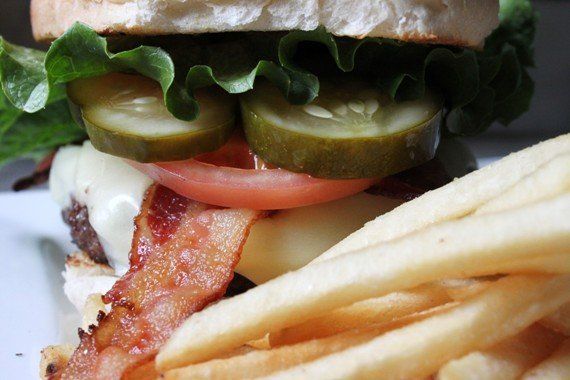 A close-up of a bacon cheeseburger with pickles, lettuce, and tomato, served with a side of french fries.