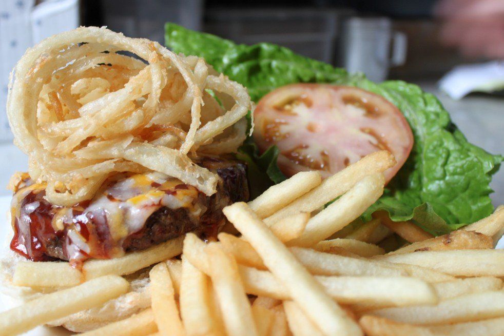 A cheeseburger topped with crispy onion strings, accompanied by a slice of tomato, lettuce, and a side of french fries.