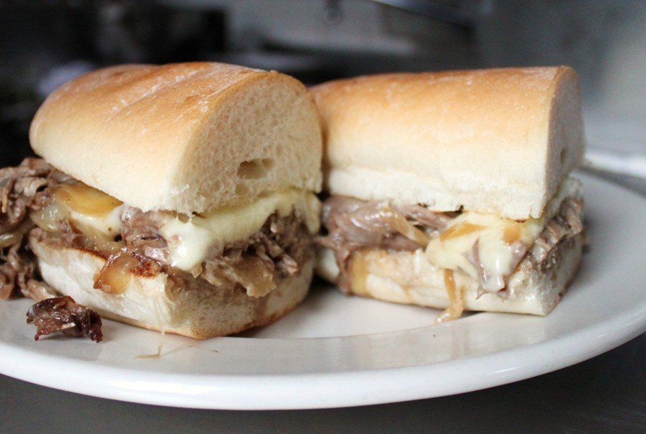 Two halves of a Philly cheesesteak sandwich with melted cheese and grilled onions on a white plate.