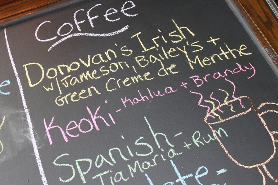 A chalkboard menu listing specialty coffee drinks, including Donovan's Irish, Keoki, and Spanish coffee with ingredients.