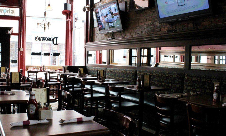 An interior view of a pub with wooden tables, chairs, dark booth seating, mirrors along the wall, and overhead TVs.