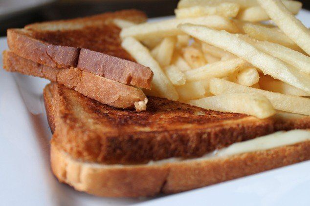 A grilled cheese sandwich cut in half, stacked on a white plate next to a pile of golden-brown french fries.