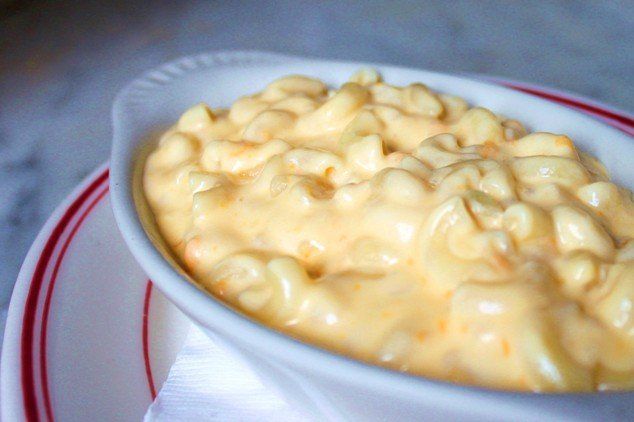 A white ceramic bowl of creamy, cheesy macaroni and cheese served on a plate with red circular trim.