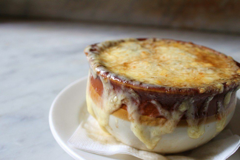 A bowl of French onion soup topped with a thick, golden-brown melted layer of cheese, resting on a white saucer.