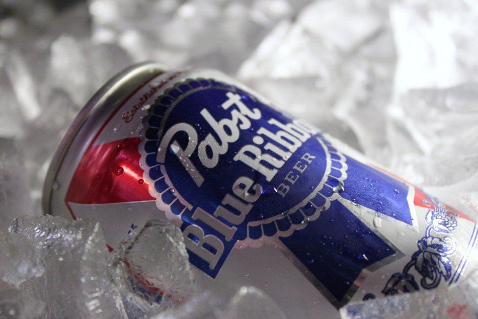 A Pabst Blue Ribbon beer can tilted on its side, surrounded by jagged ice cubes.