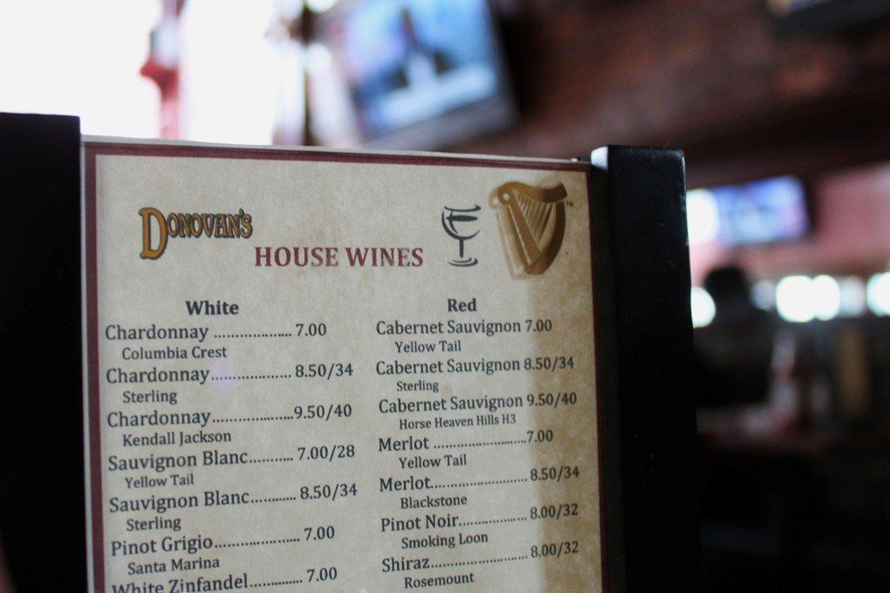 A Donovan’s restaurant menu listing house white and red wines with prices, held in a dim, blurred pub setting.