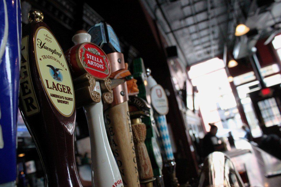 A close-up of a row of beer tap handles in a dimly lit bar, with a Stella Artois tap prominent in the center.