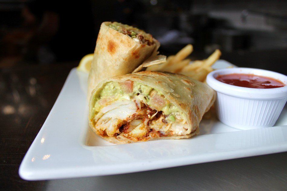 A plate with two halves of a chicken and avocado wrap, served with french fries and a small side of dipping sauce.