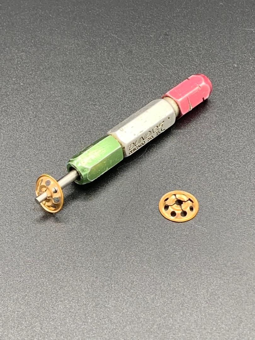 A green , red and white pencil is sitting on a table next to a small gold object.