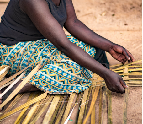 A woman is sitting on the ground making a basket