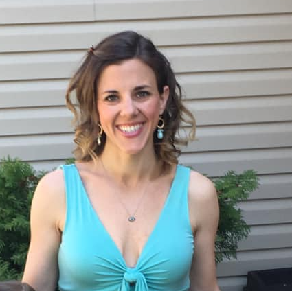 A woman in a blue tank top and earrings is smiling for the camera.