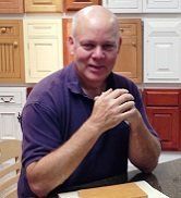 A man is sitting at a table in front of a wall of cabinets.