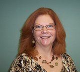 A woman with red hair and glasses is smiling for the camera.
