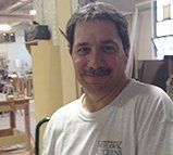 A man with a mustache is wearing a white t-shirt and smiling in a room.