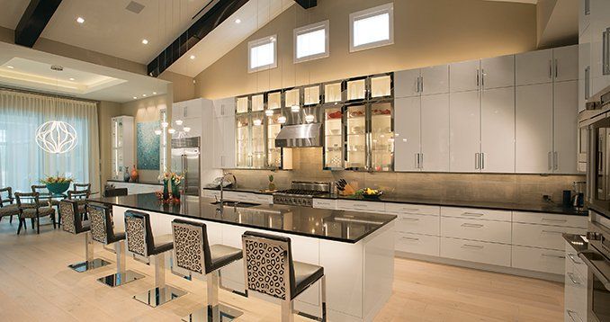 A large kitchen with white cabinets and black counter tops and stools.