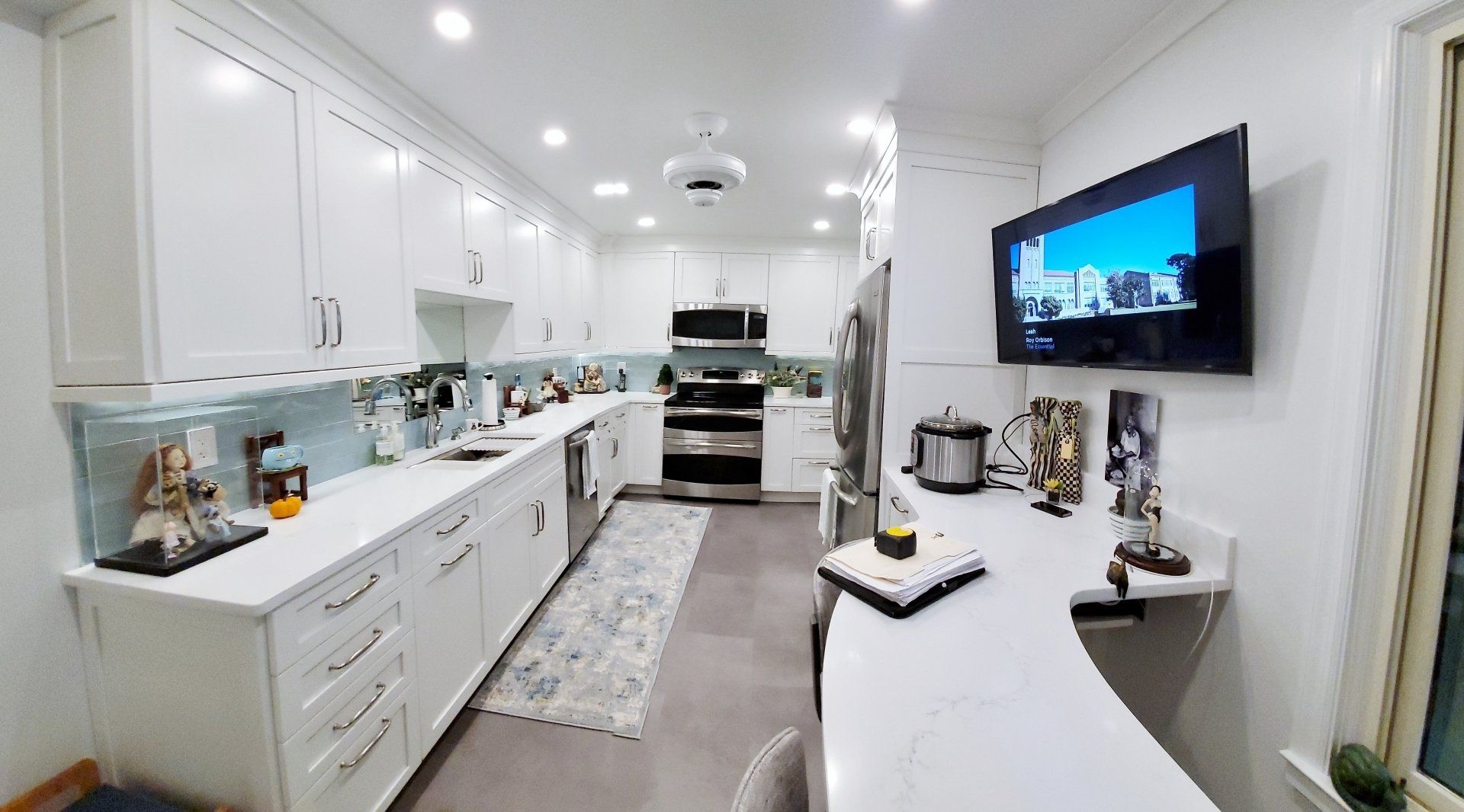 A kitchen with white cabinets and stainless steel appliances and a flat screen tv hanging on the wall.