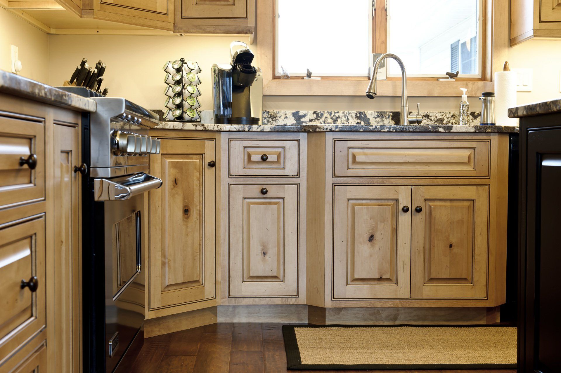 Compact kitchen with light wood cabinets, granite countertops, and a stainless steel sink under a window