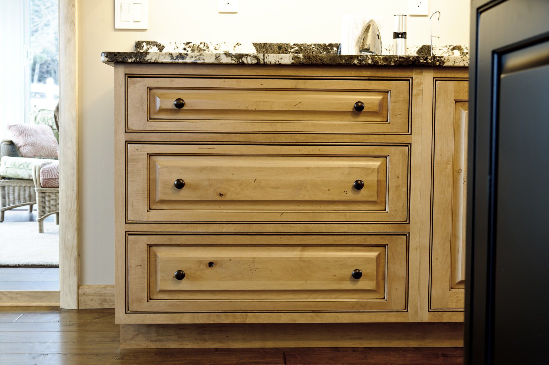 Wooden bathroom vanity with three drawers and granite countertop beside a mirror.