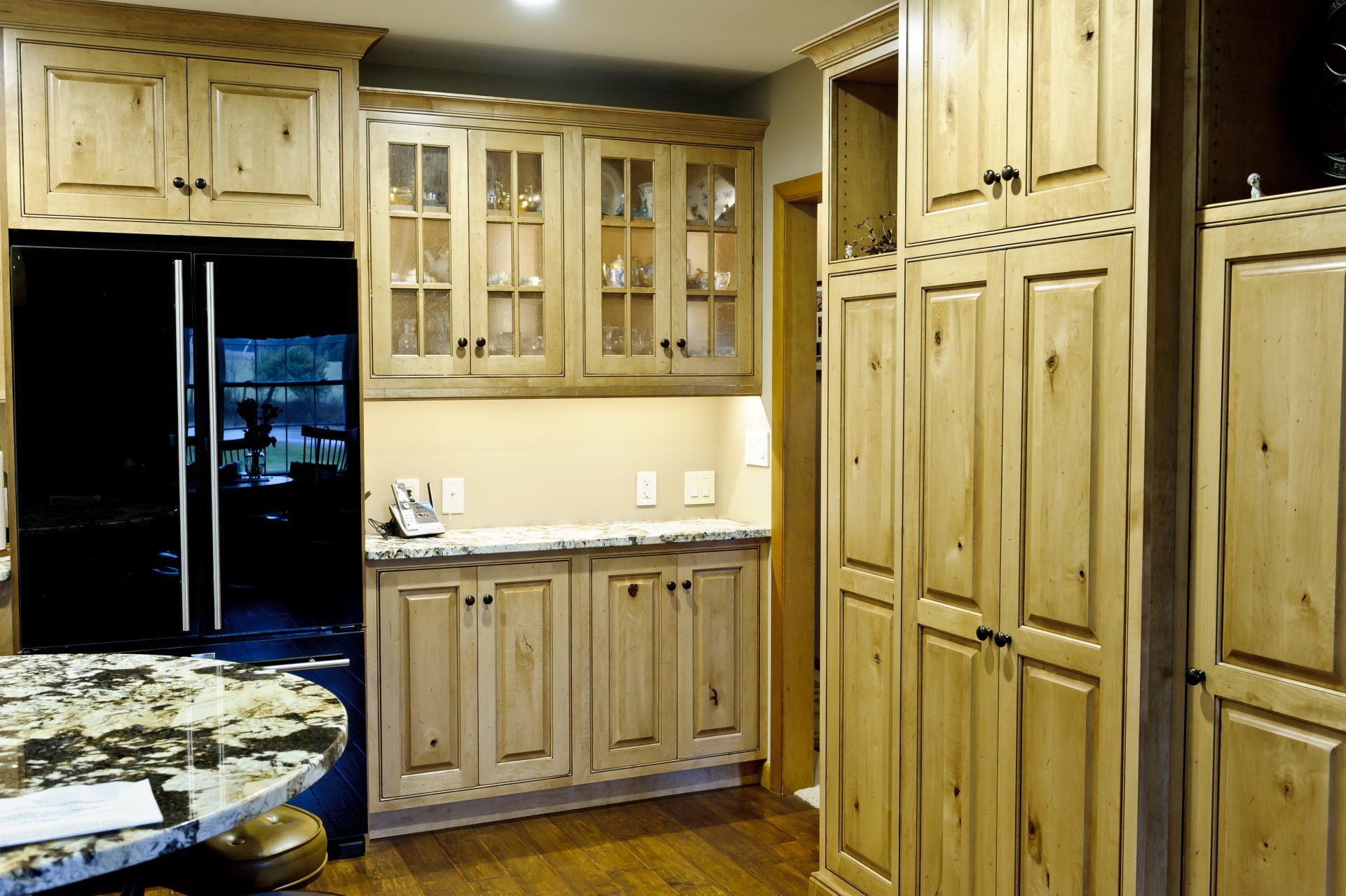 Wooden kitchen with black refrigerator, glass-front cabinets, and built-in pantry cupboards