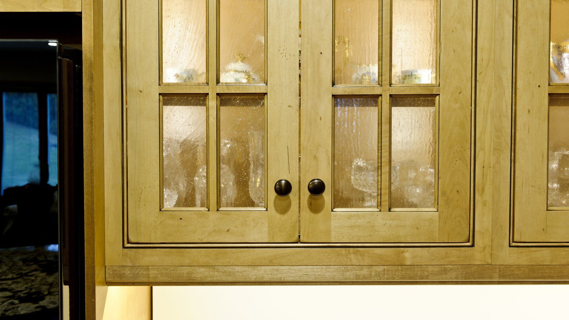 Wooden kitchen cabinets with frosted glass doors and black knobs in warm lighting