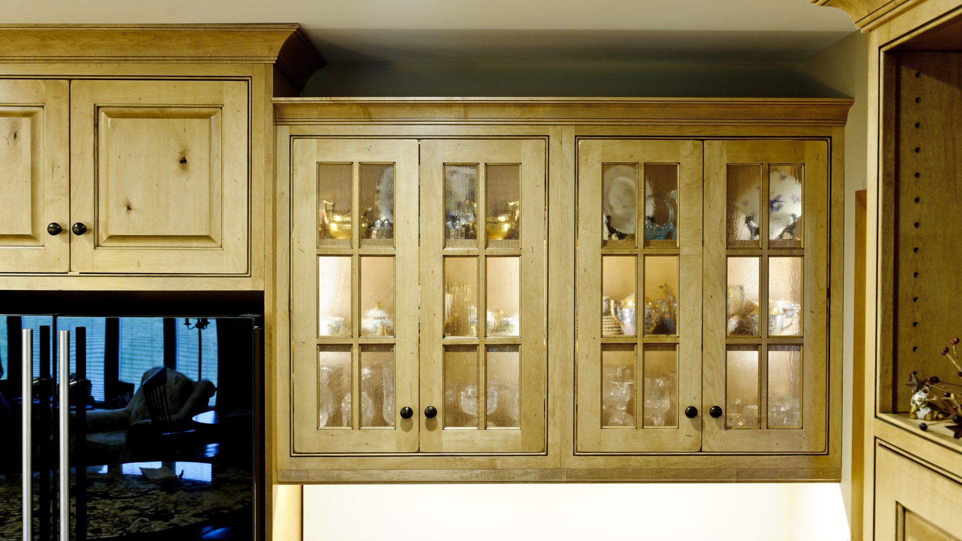 Kitchen with light wood cabinets, glass-front doors, and a black refrigerator on the left.