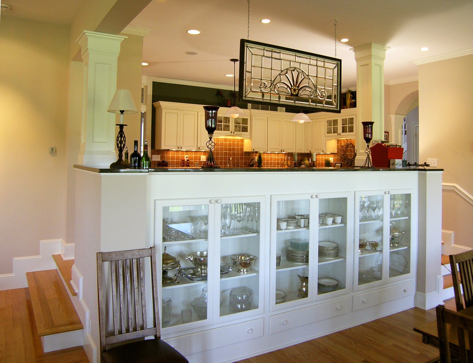 White kitchen island with glass cabinet doors and a breakfast bar in a bright open-plan home