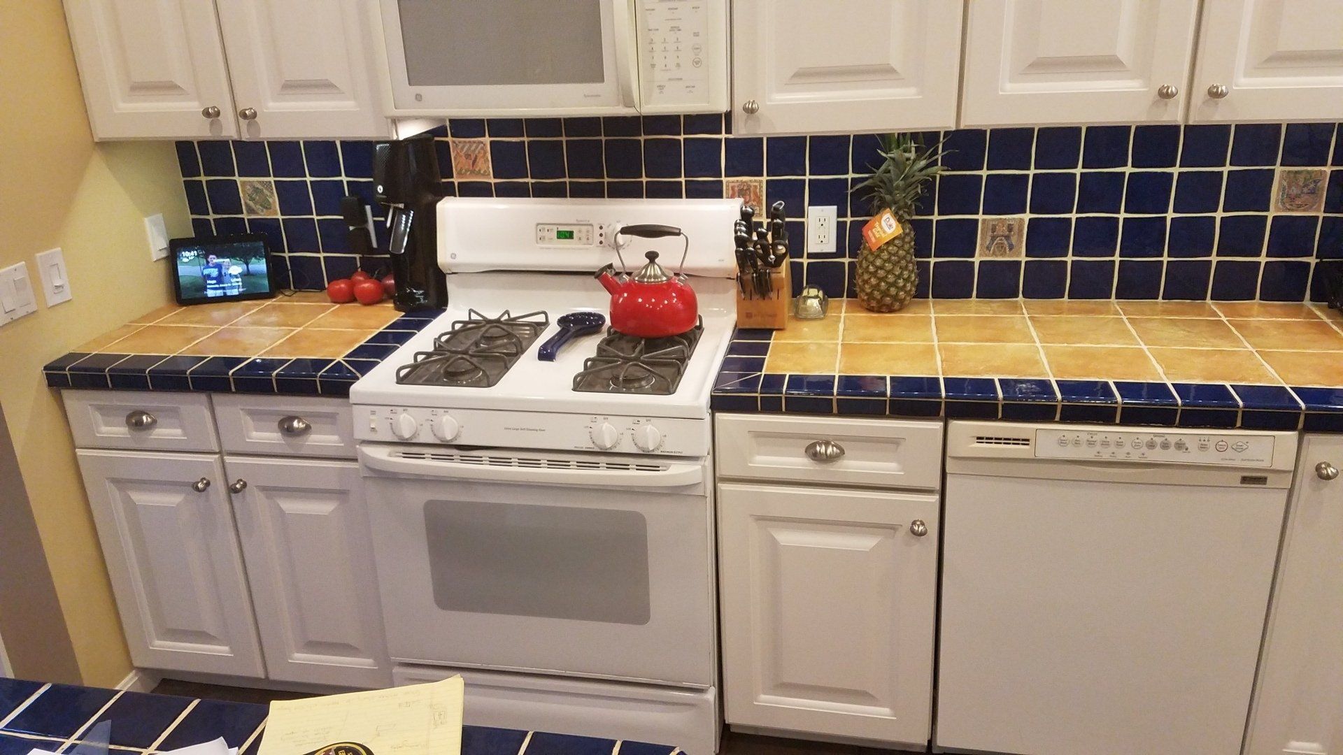 Kitchen with white cabinets, blue tile backsplash, gas stove, dishwasher, and wooden countertops.