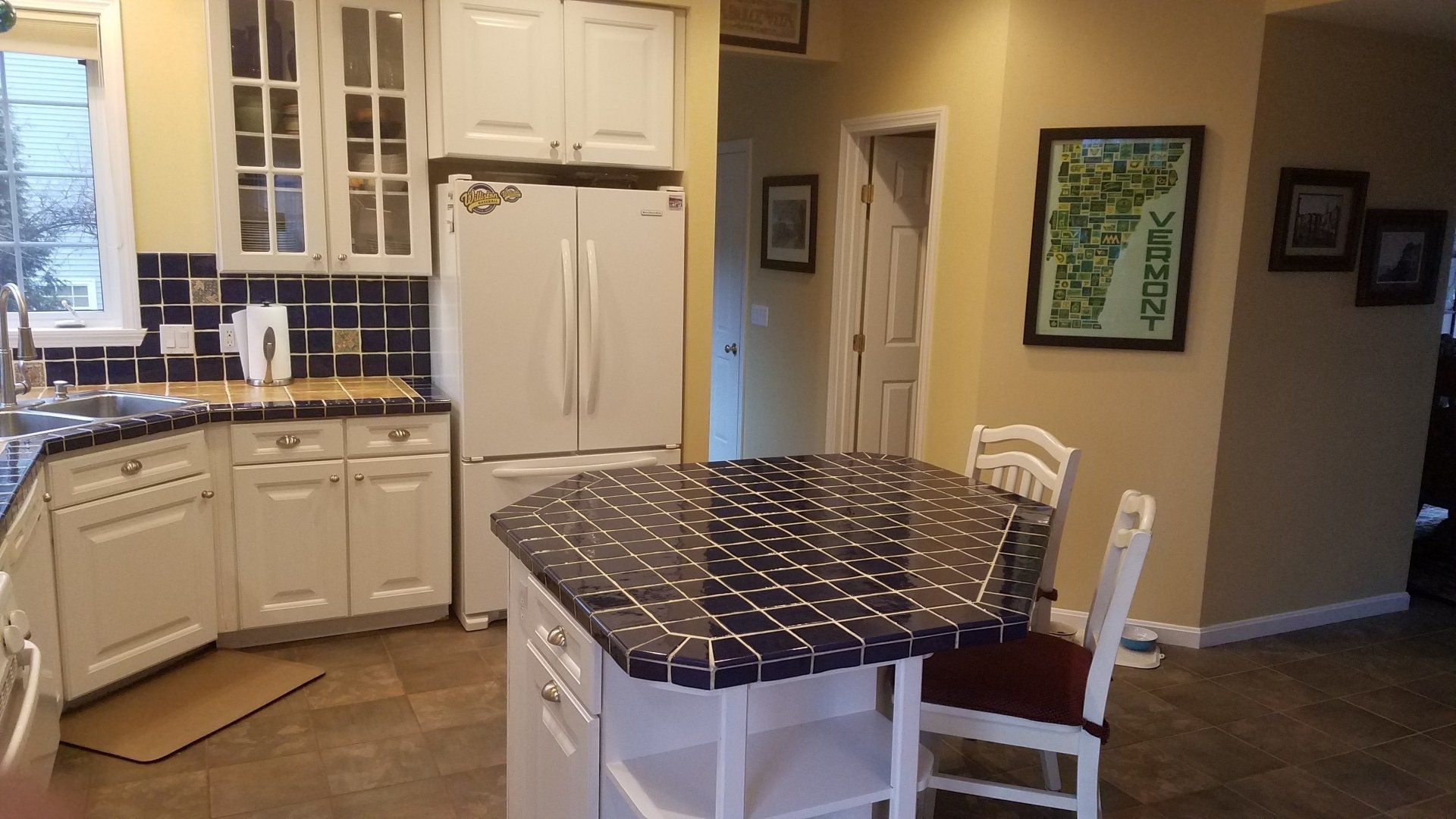 Bright kitchen with white cabinets, black countertops, and a small island with a patterned tablecloth.