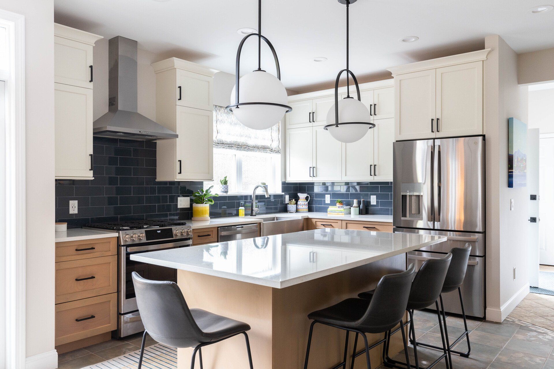 Modern kitchen with white cabinets, black backsplash, stainless fridge, and a marble island with black chairs