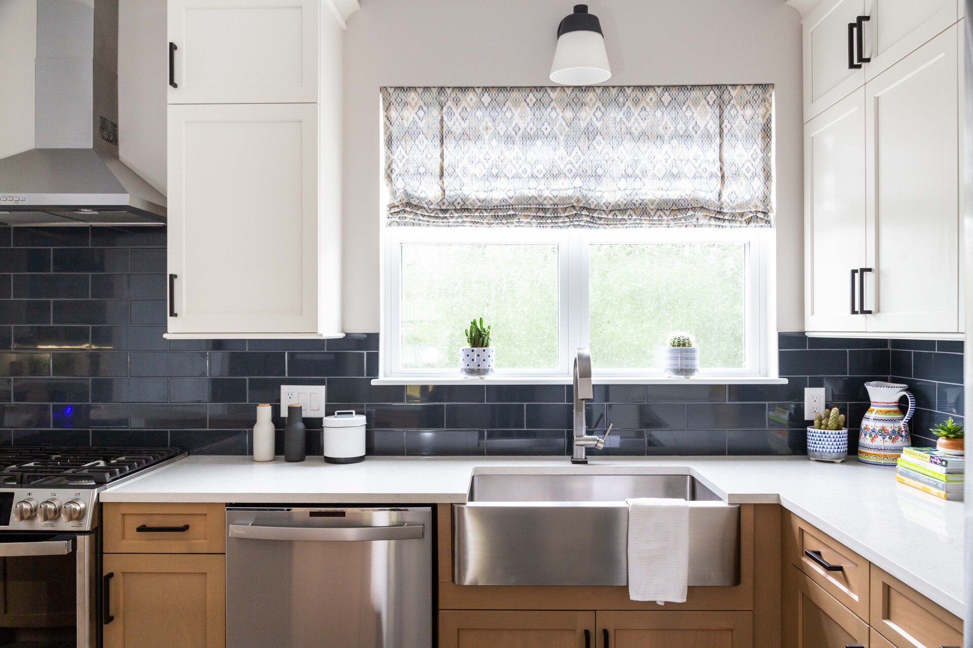 Modern kitchen sink beneath a window, with white cabinets, dark tile backsplash, and stainless steel appliances