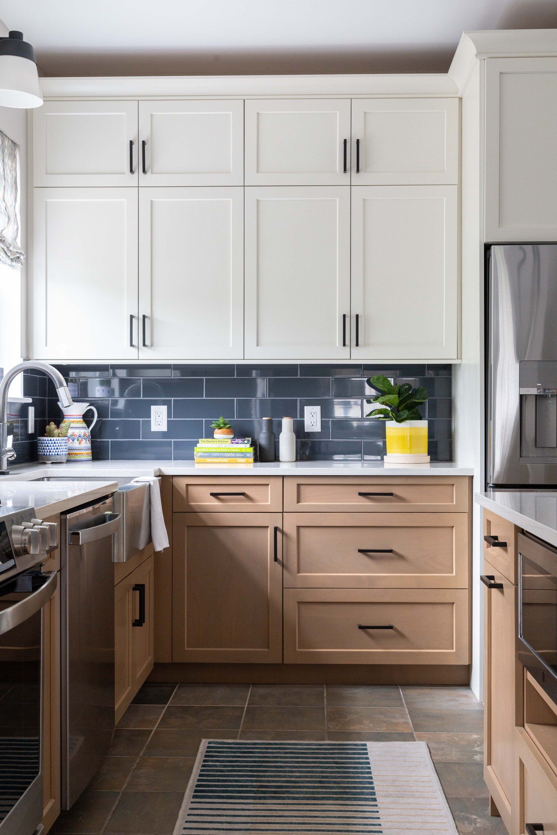 Bright kitchen with white upper cabinets, wood lower cabinets, dark backsplash, and stainless steel appliances