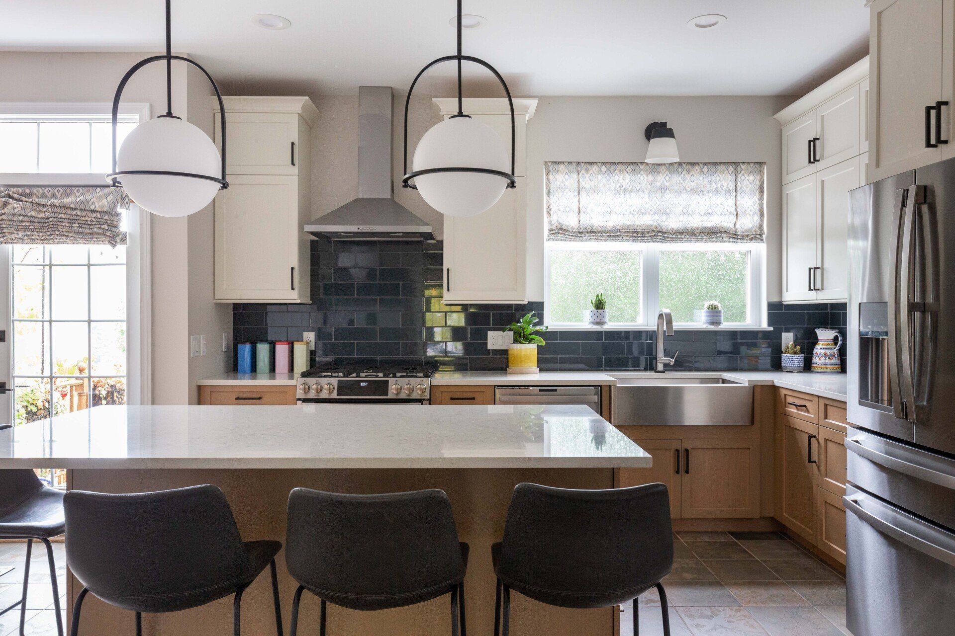 Modern kitchen with island, black stools, cream cabinets, and pendant lights
