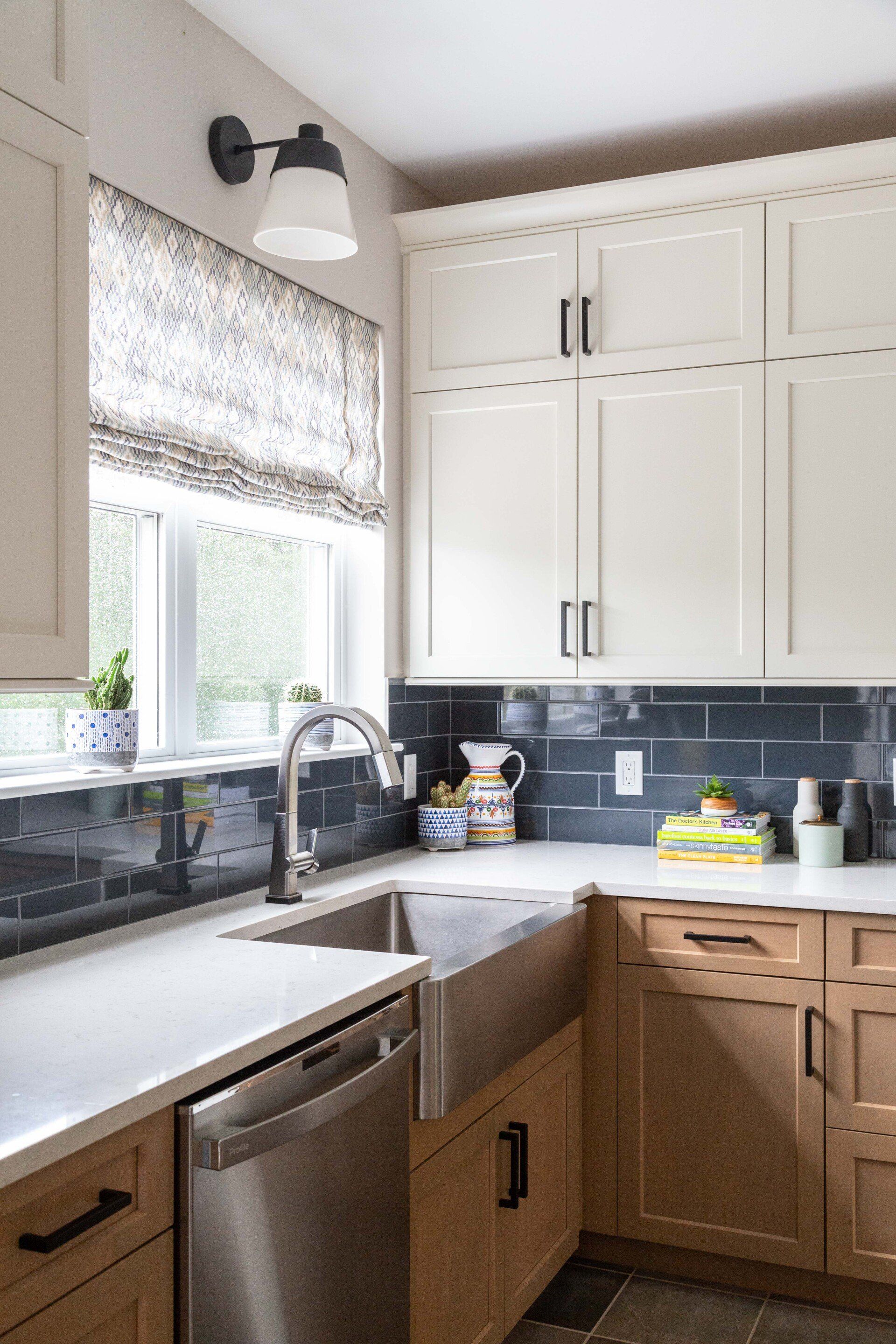 Bright kitchen corner with white cabinets, gray tile backsplash, sink, and window with a patterned shade.
