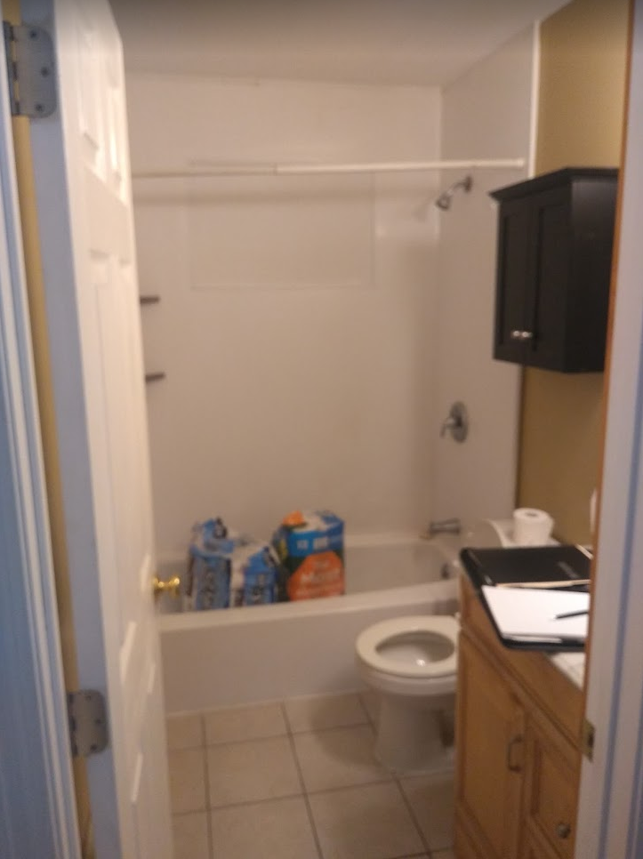 Small bathroom with a tub, toilet, sink cabinet, and toiletries on the floor.