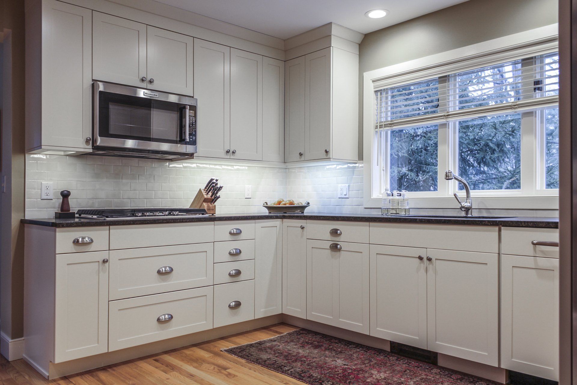 Bright modern kitchen with white cabinets, stainless microwave, and a window over the sink