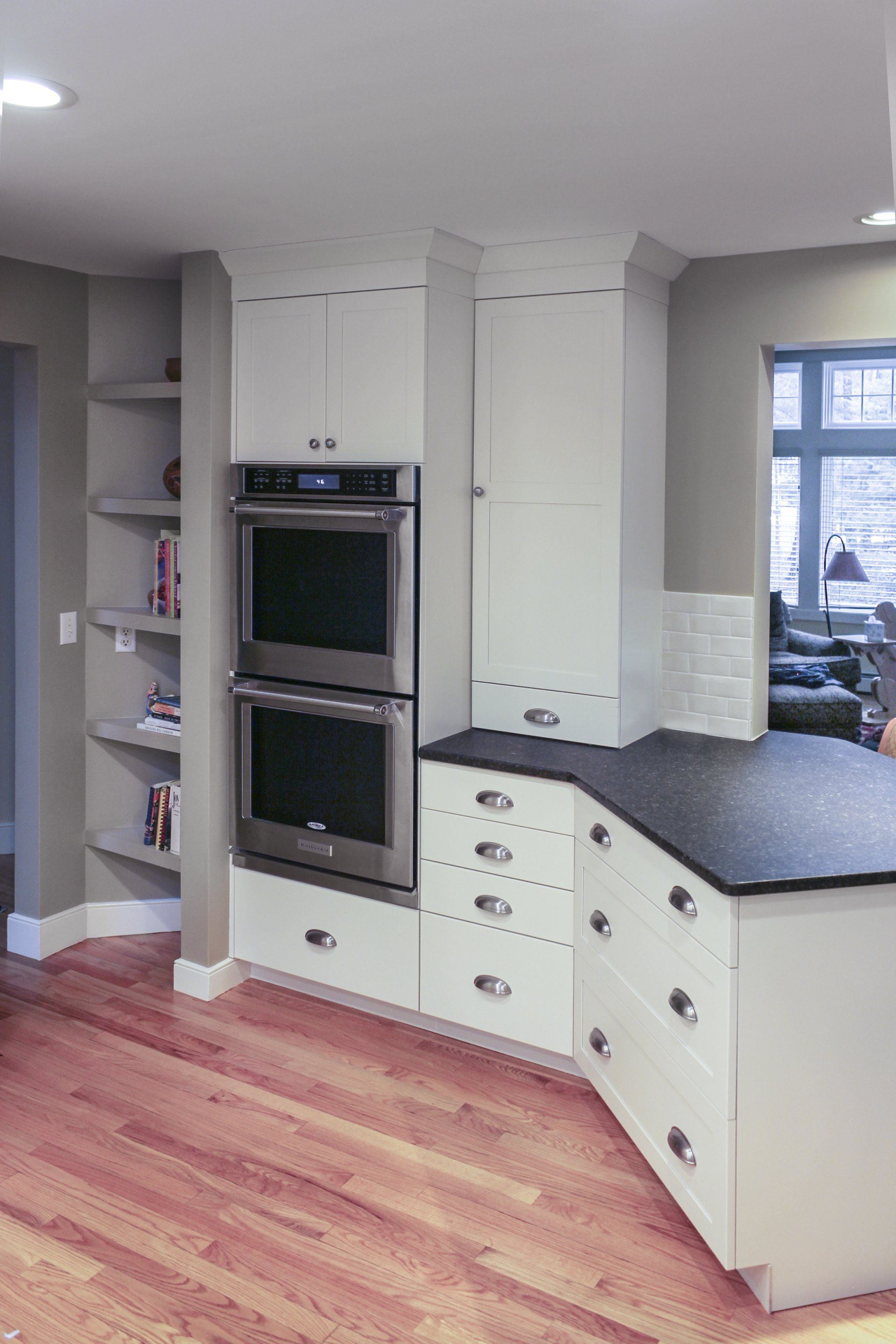Modern kitchen with built-in ovens, white cabinets, dark countertops, and hardwood floors