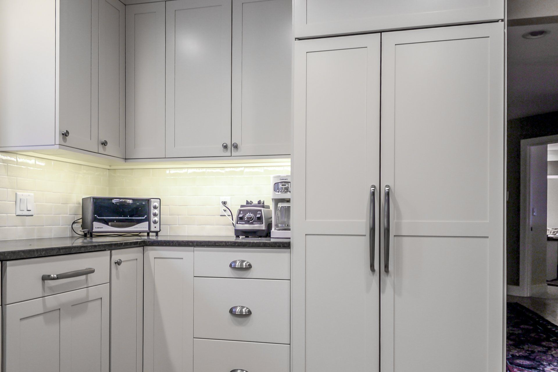 Modern white kitchen with gray cabinets, stainless appliances, and under-cabinet lighting.