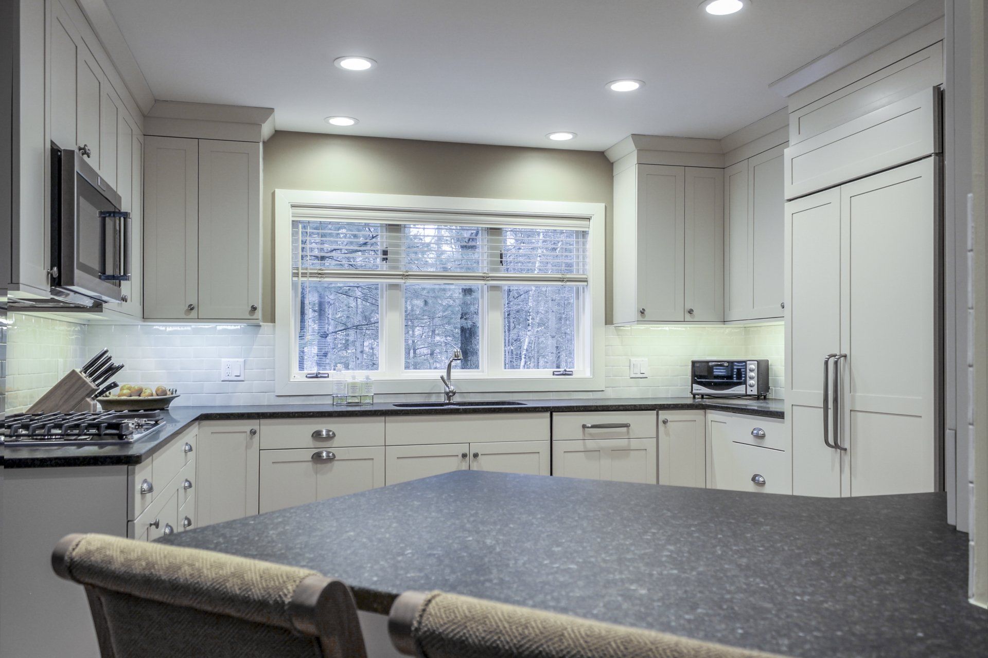 Modern white kitchen with large window, gray island countertop, and stainless steel appliances