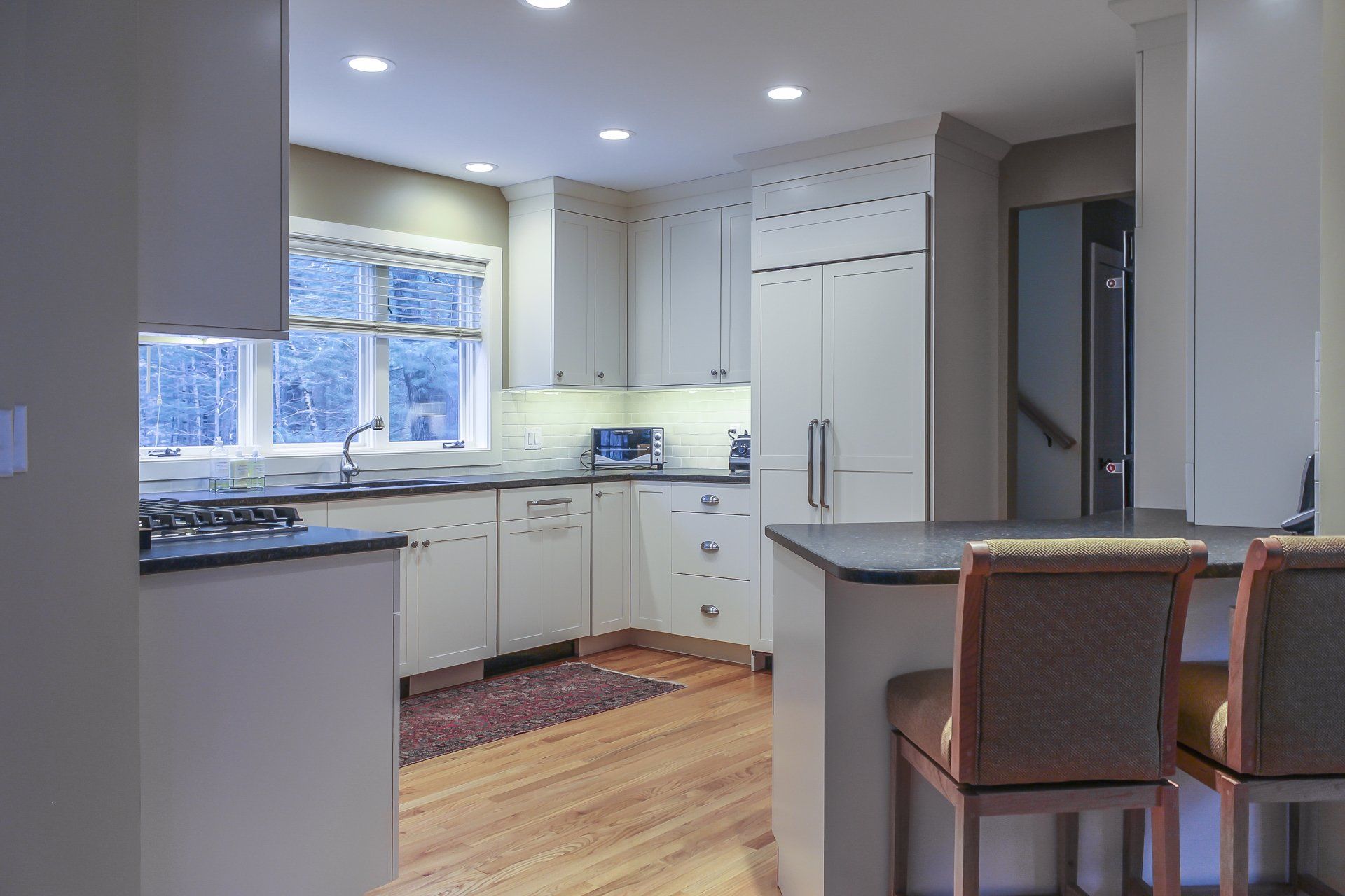 Bright modern kitchen with white cabinets, stainless appliances, and two stools by a breakfast counter.