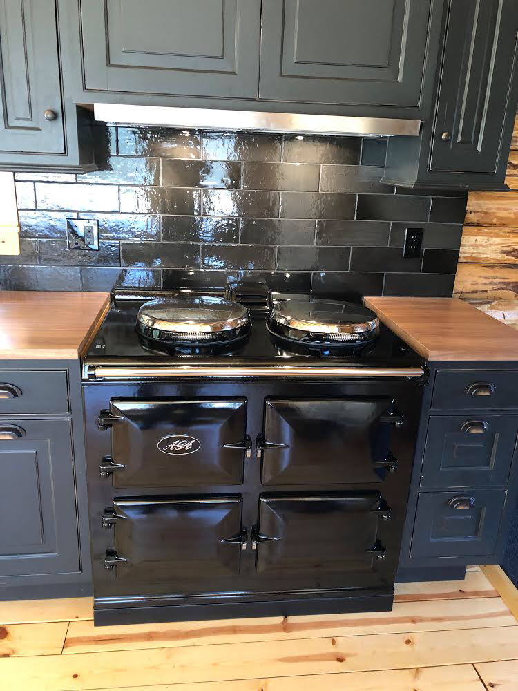 Black vintage stove between dark cabinets in a kitchen with stainless backsplash and wood countertops