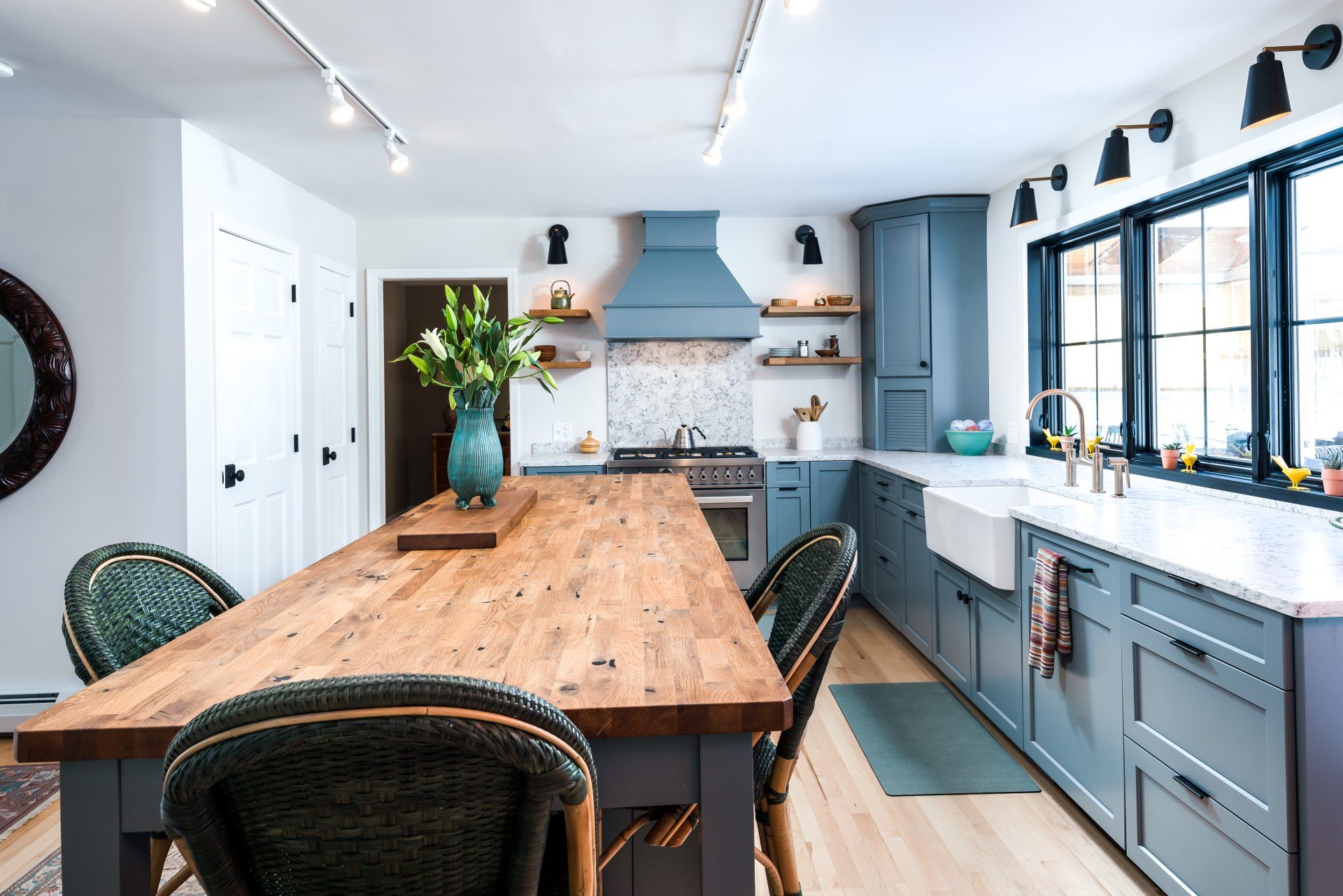 Bright kitchen with a long wooden table, blue cabinets, and large windows letting in daylight