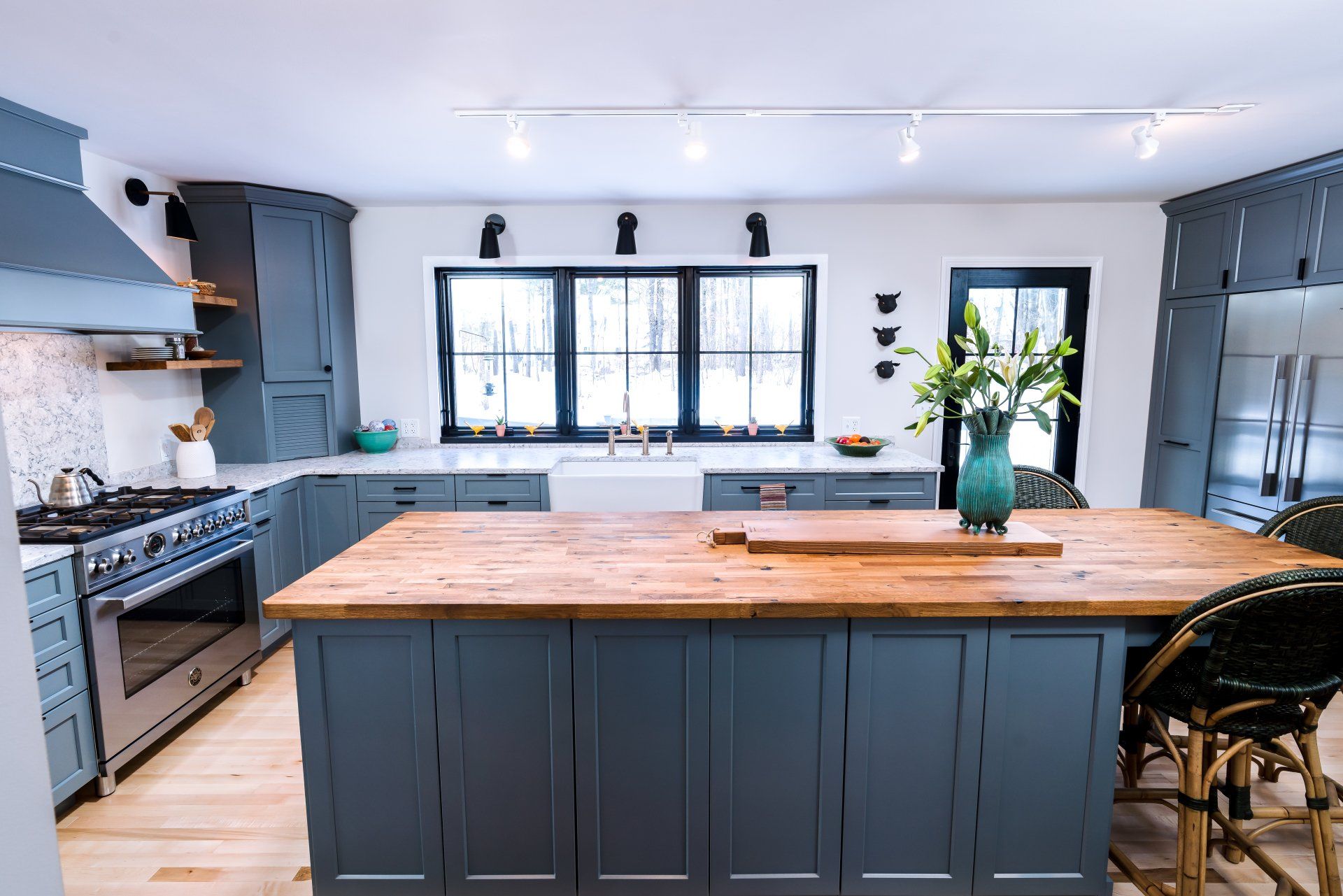 Modern kitchen with large wooden island, gray cabinets, black stove, and bright windows