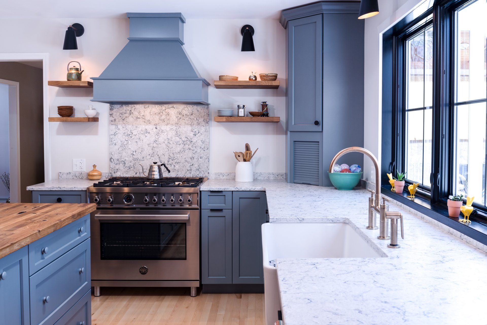 Modern blue-and-white kitchen with marble counters, stainless stove, tiled backsplash, and large windows