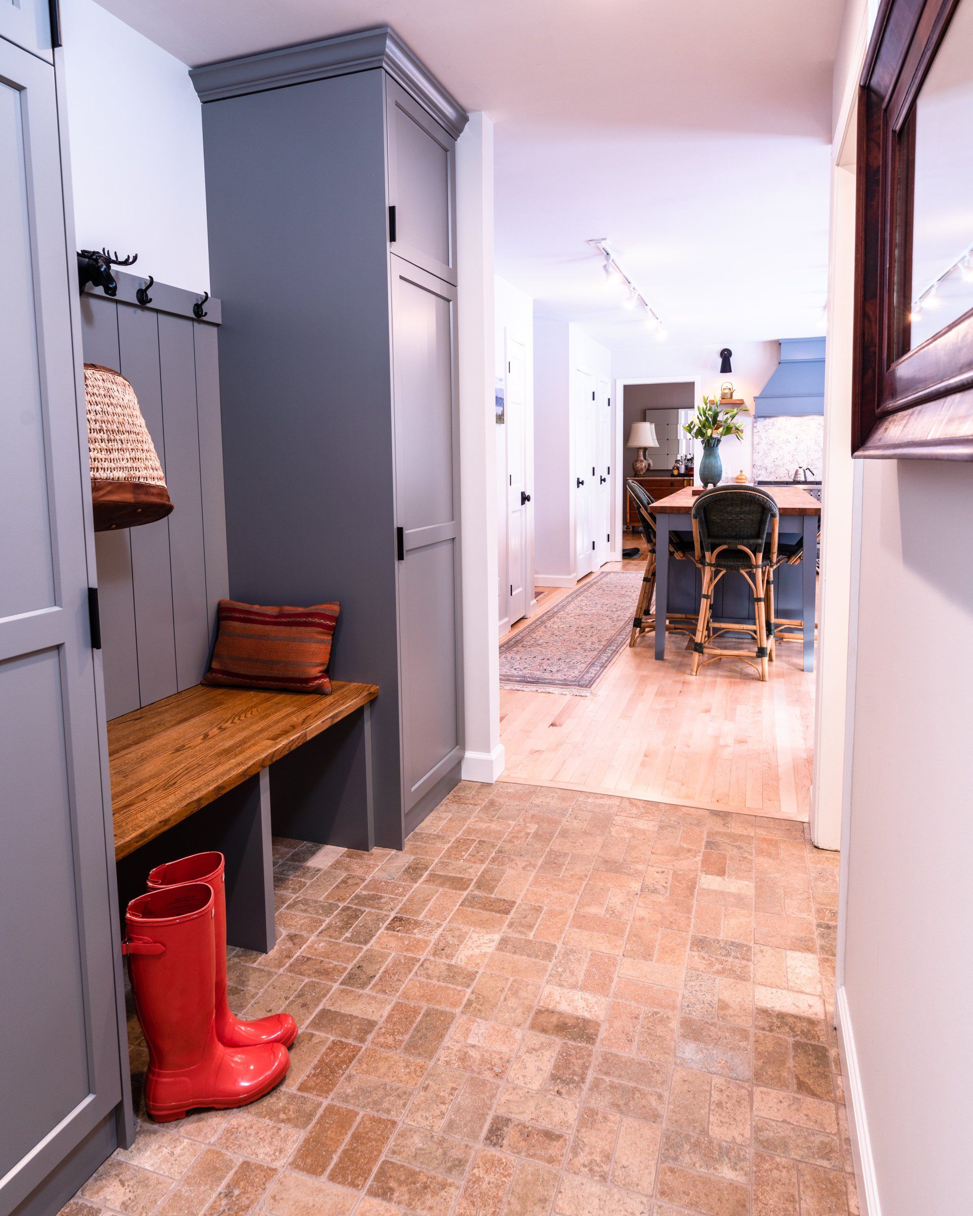 Narrow hallway with a bench and red rain boots leading to a bright dining room