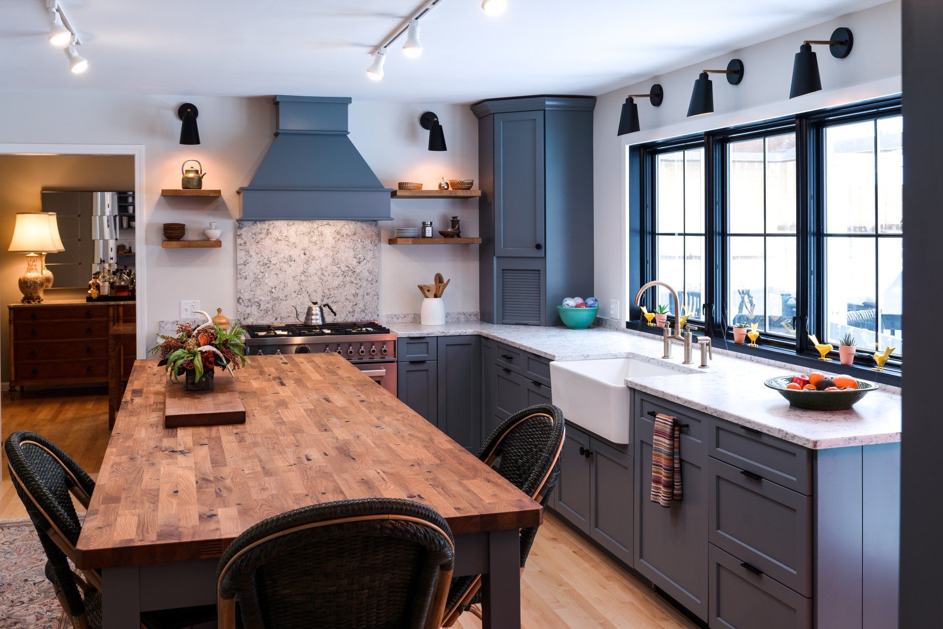 Bright modern kitchen with wood island, gray cabinets, blue range hood, and large windows